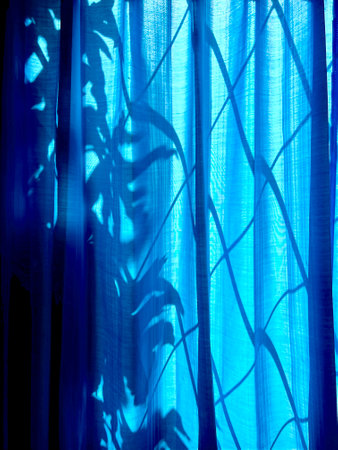 sunlight through a blue curtain in the room with shadow on the wallの写真素材
