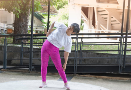 Old lady bend side of body for stretching before exercise,outdoor activity,blurry light aroundの写真素材
