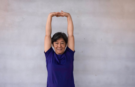 Old lady clasp hands over head for stretching body before exercise,with happy feeling,blurry light...