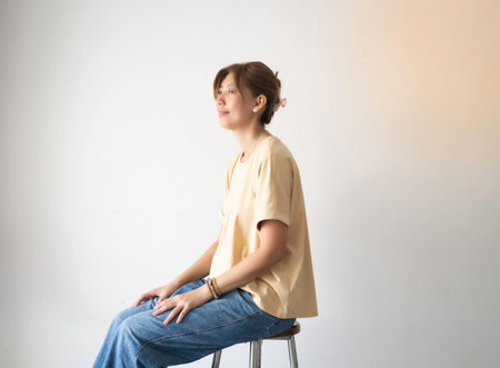 Woman wearing cream T-shirt and blue jeans sitting againt from wall,with happy feeling,portrait model posingの写真素材