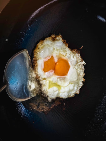 Stainless Spatula touch of Sunny side fried egg in black chinese wok,homemade cookingの写真素材
