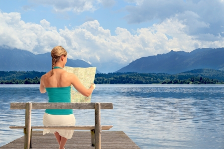 A young woman reading a map sitting on a bench in front of a lakeの写真素材