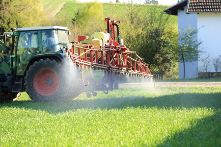 A Tractor spraying pesticide near housesの写真素材