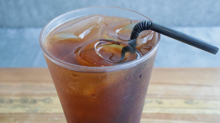 A tall glass of ice tea with a straw on the table.の写真素材