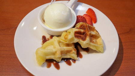 Waffle with vanilla ice cream topping and strawberry slice with chocolate sauce dessert served on white plate.の写真素材
