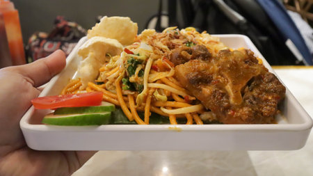 Indulge in oxtail fried noodle, served with crunchy crackers, and garnished with fresh cucumber and tomato slices.の写真素材