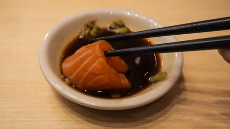 Hand is dipping salmon sushi into Shoyu sauce using chopsticks.の写真素材
