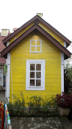 Charming Yellow Wooden House Facade with White Trim and Rustic Window, Surrounded by Lush Greenery in a Quaint Village Settingの写真素材