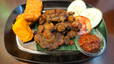 Spicy Grilled Oxtail with Tofu and Tempeh Served with Fresh Cucumber and Tomato Slices and Spicy Chili Sauce on Black Plateの写真素材