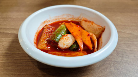 Korean Banchan with Assorted Vegetables in Spicy Red Sauce in a White Ceramic Bowl on Wooden Tableの写真素材
