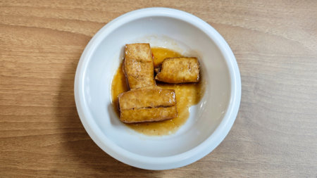 Korean Banchan with Pan-Fried Tofu Served in a White Ceramic Bowl on Wooden Tableの写真素材