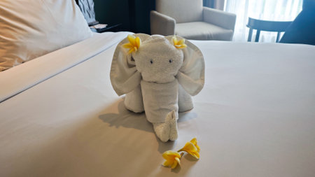 Elegant Elephant-Shaped Towel Art on a Neatly Made Hotel Bed with Frangipani Flowers in a Relaxing Tropical Resort Roomの写真素材