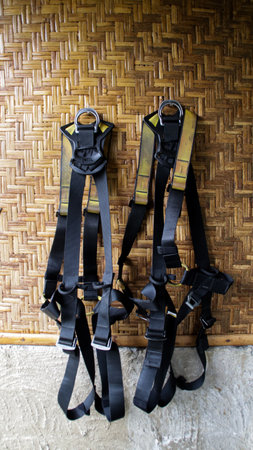 Two Black Climbing Harnesses Hanging Against Bamboo Wall in Rustic Outdoor Setting