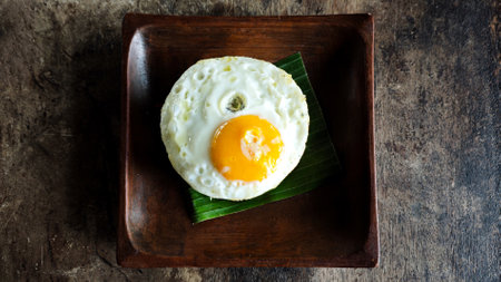 Top View of a Perfectly Cooked Sunny Side Up Egg on Banana Leaf in a Wooden Square Plate with Rustic...