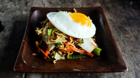 Traditional Indonesian Stir-Fried Noodles Topped with a Fried Egg on a Wooden Plate with Rustic Backgroundの写真素材
