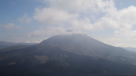 Cloud-covered Mount Batur under a clear blue sky with scenic volcanic landscape and rugged terrain in Kintamani Bali Indonesiaの写真素材