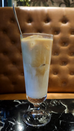 Refreshing iced latte in a tall glass served on a black marble table with a brown tufted leather...