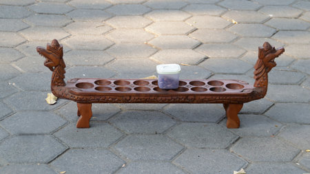 Hand-Carved Wooden Congklak Game Board with Dragon Head Design on Stone Pavement Background in Outdoor.の写真素材