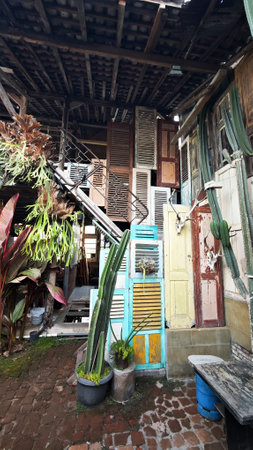 Colorful rustic outdoor wall made from repurposed wooden shutters and doors with cactus plants, iron staircase, and brick patio under a wooden roof.の写真素材