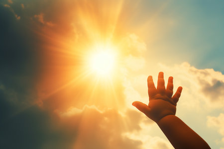 Hand of a child reaching up to the sun on a background of blue skyの素材