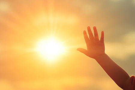 Child hand on sunset sky background. Freedom concept. Copy space.の素材
