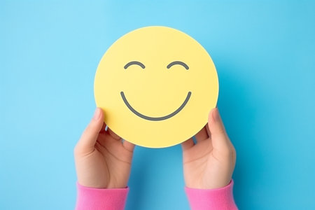 Woman holding yellow sticker with smiley face on blue background, top viewの素材