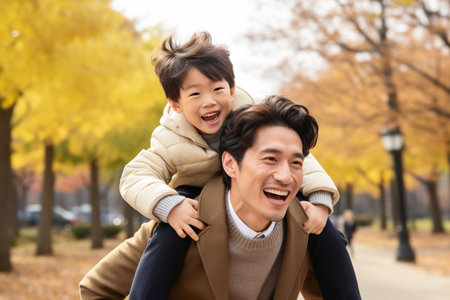 Happy asian family having fun in autumn park. Father carrying son on shouldersの素材