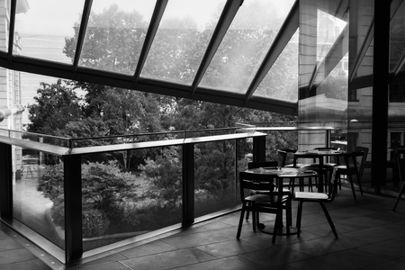black and white picture of cafe table and chairs standing on a balcony of a trade center under a glass roofの写真素材