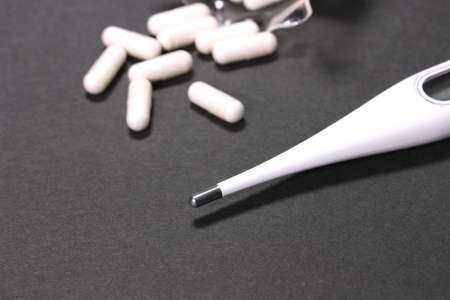 Capsules and thermometer on black background