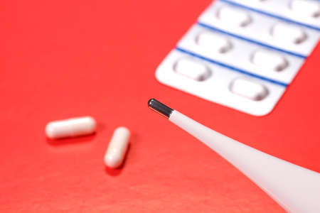 Capsules and thermometer on red background