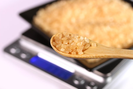 Brown cane sugar on a square plate on kitchen scale and wooden spoonの写真素材