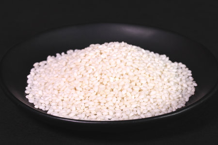 <p>Uncooked japanese sticky rice on a plate on black background</p>の写真素材