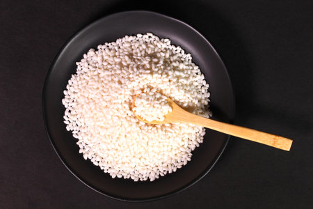 Uncooked japanese sticky rice on a plate and wooden spoonの写真素材