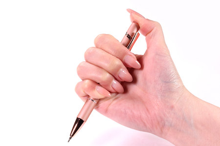 Female hand with pink manicure holding a pen isolated on white backgroundの写真素材