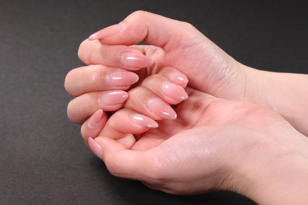 Female hands with pale pink manicure on nails, isolated on blackの写真素材