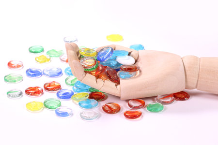 Wooden hand holding a lot of colorful glass marbles on white backgroundの写真素材