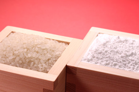 White rice and rice flour in a wooden box on red backgroundの写真素材
