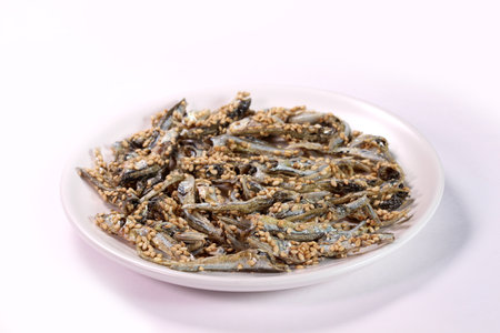 Fried anchovies with sesame seeds on a plate on white background.の写真素材