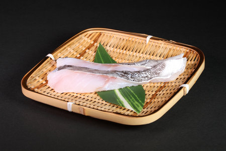 Cod fillet on bamboo colander on black backgroundの写真素材