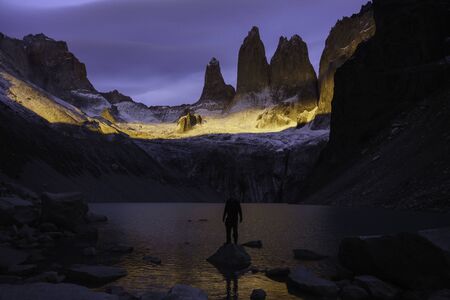 Torres del Paine peaks illuminated with the sunrise. A person posing at the base of the mountain and a small lagoon and rocks around them. Patagonia, Chileの写真素材