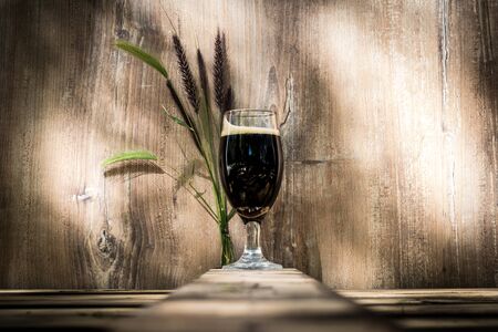 Glass of black beer with foam. Wooden background with streaks and spikes behind.の写真素材