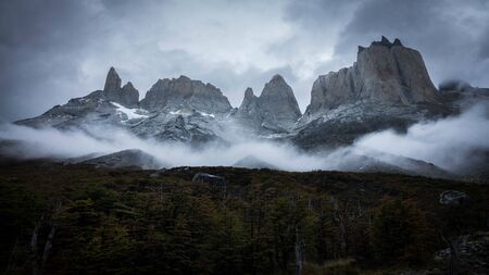 Beautiful mountain landscape full of clouds and fog. There are large snowy peaks seen from a thick forest. Torres del Paine trail, Patagonia, South Americaの写真素材