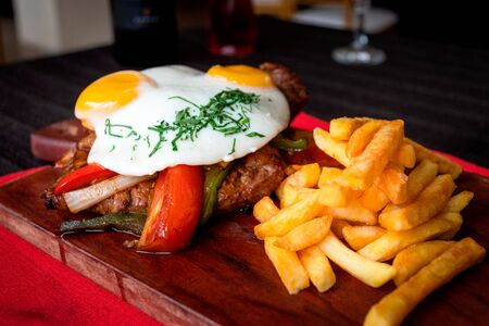 Juicy meat accompanied with sauteed vegetables fried egg and french fries, all served on a wooden boardの写真素材