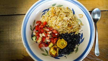 Plate with rice, black beans, fried banana and a tomato and cucumber saladの写真素材