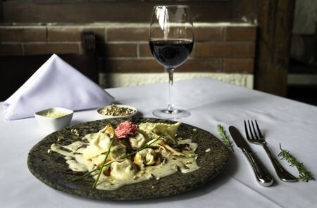 Tortellini pasta with white sauce served on a marble plate with a glass of wine and cuttery. Rustic Italian backgroundの写真素材