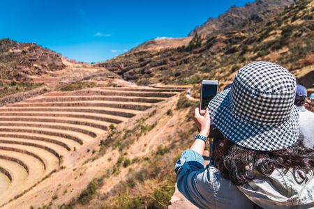 A tourist woman taking a picture of the ruins of Pisac with her smartphone in the Sacred Valley of the Incas. Cusco region, Peru.の写真素材