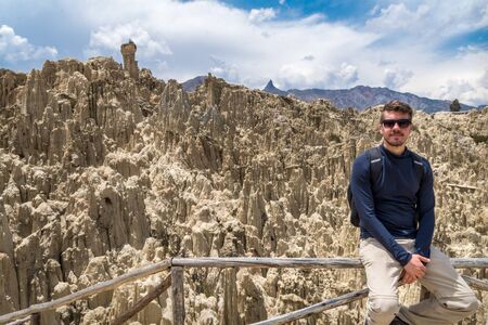 A tourist man posing in the Moon Valley in La Paz, Bolivia. Many clay peaks can be seen on the backgroundの写真素材