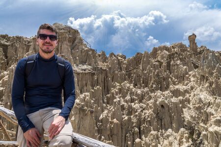 A tourist man posing in the Moon Valley in La Paz, Bolivia. Many clay peaks can be seen on the backgroundの写真素材