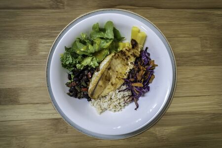 Grilled fish, salad, rice and beans served on a white plate on a wooden backgroundの写真素材