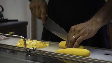 Chef cutting with a big knife yellow zucchini on a tableの写真素材